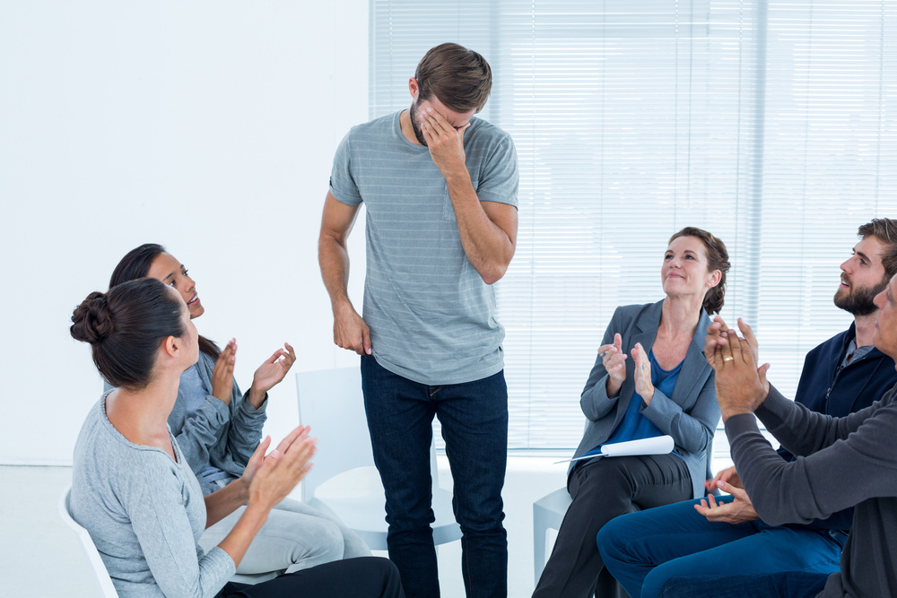 Rehab group applauding delighted man standing up at therapy session