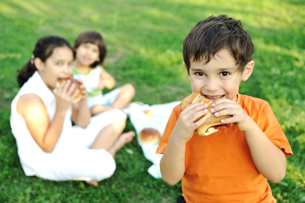 Small group of children in nature eating snacks together, sandwiches, bread